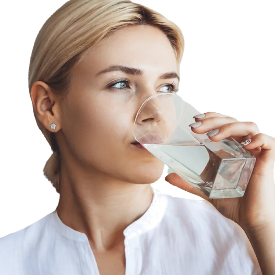 Woman drinking a glass of filtered water at a kitchen sink